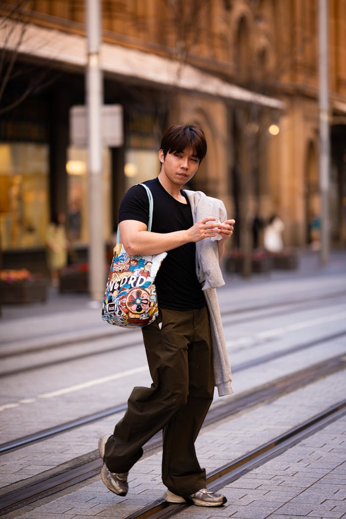 Services Man walking in city, holding phone, carrying a colorful bag. Urban lifestyle scene.