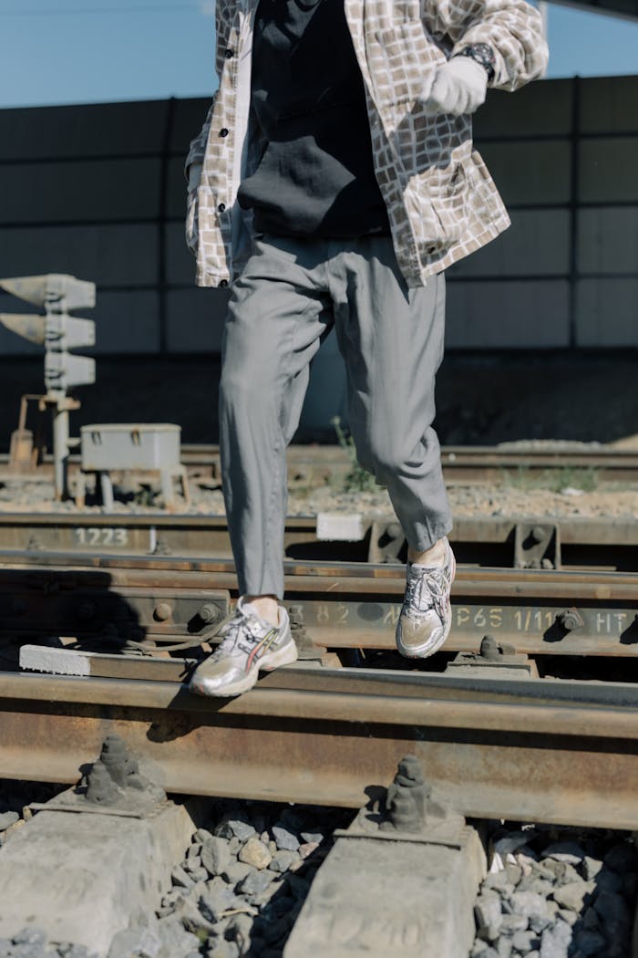Services A close-up of a person in sneakers walking on train tracks, emphasizing movement and fashion in an urban setting.
